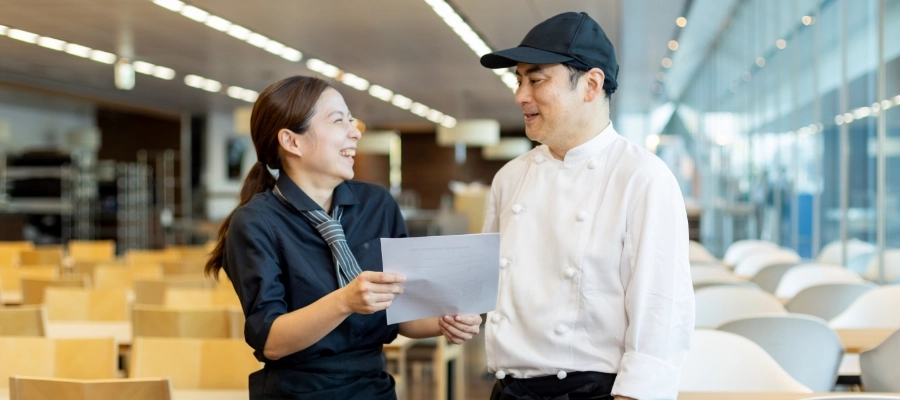 O.N.さん仕事風景　管理栄養士と書類を見ながら会話している写真