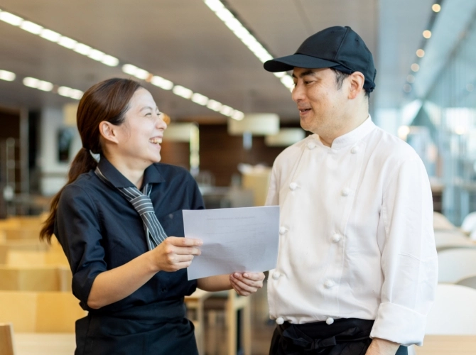 O.N.さん仕事風景　管理栄養士と書類を見ながら会話している写真