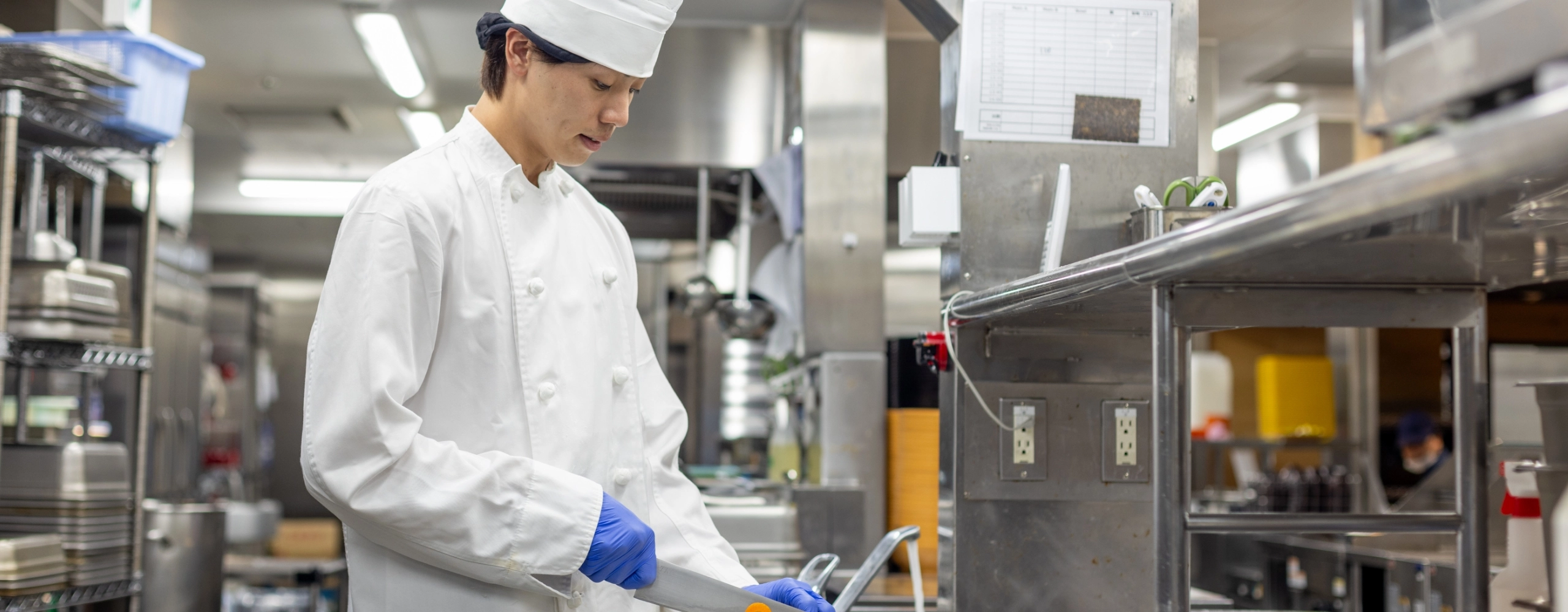 H.M.さんインタビューキービジュアル　厨房で包丁を使っている写真