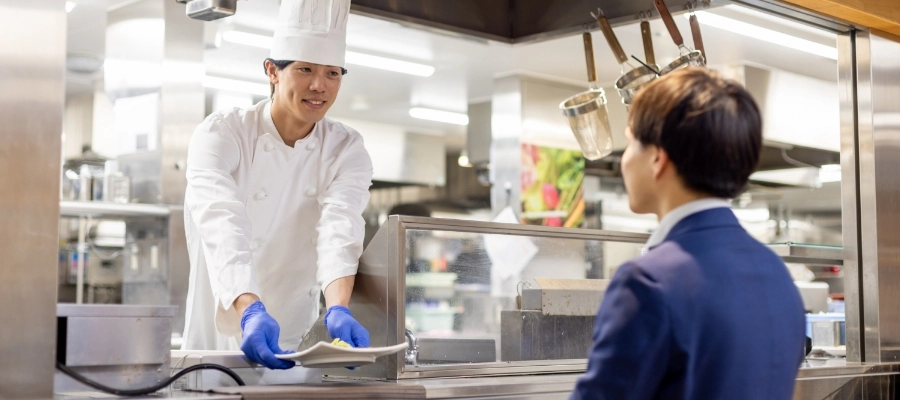 H.M.さん仕事風景　厨房のカウンターから出来上がった料理を提供している写真