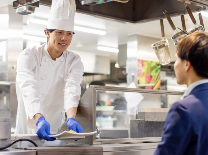 H.M.さん仕事風景　厨房のカウンターから出来上がった料理を提供している写真