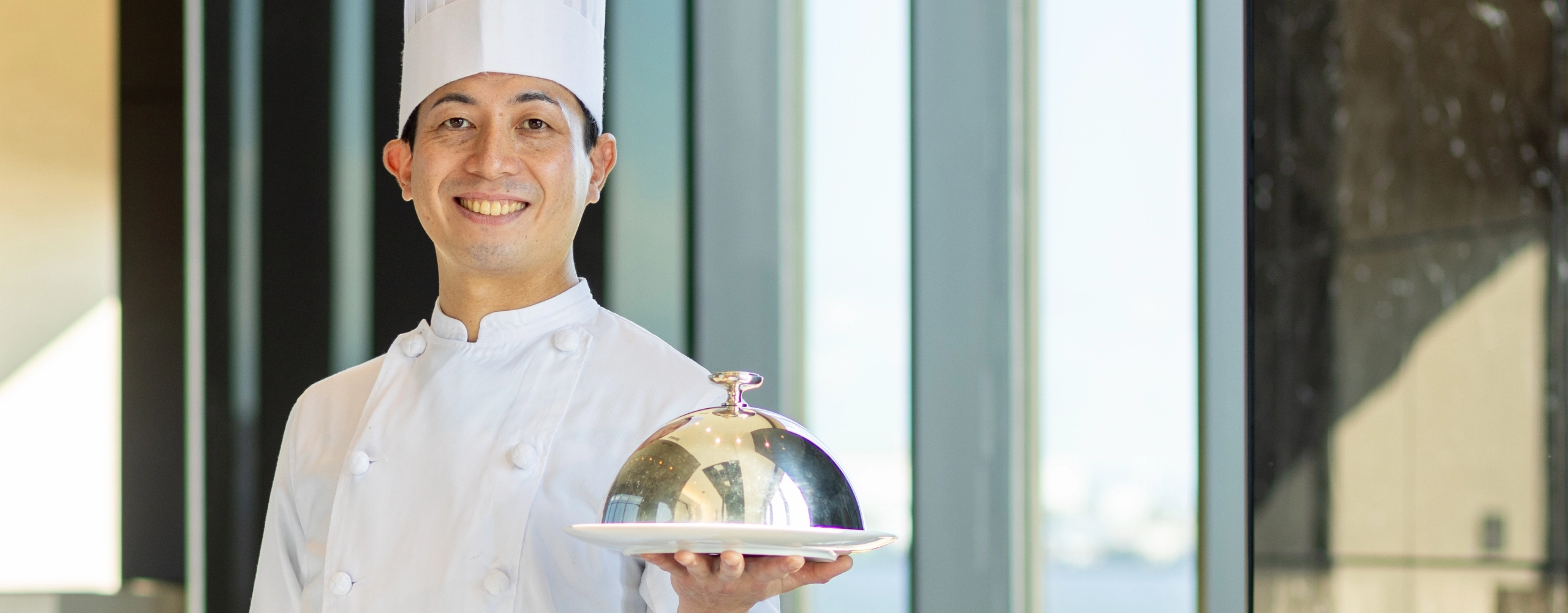 N.T.さんインタビューキービジュアル　ホールでお皿を持って笑顔で立っている写真