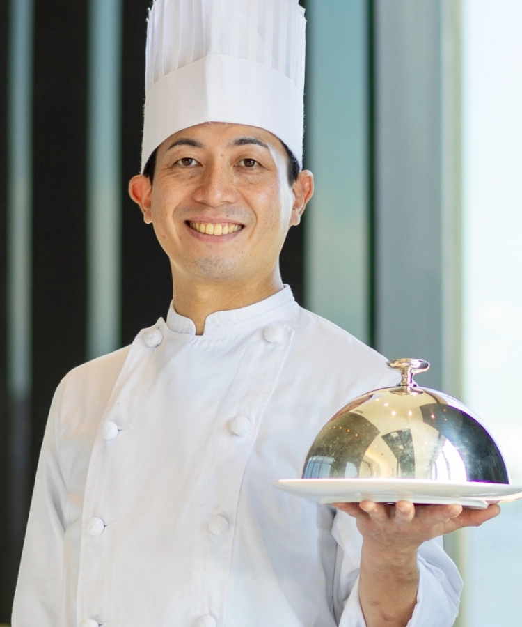 N.T.さんインタビューキービジュアル　ホールでお皿を持って笑顔で立っている写真