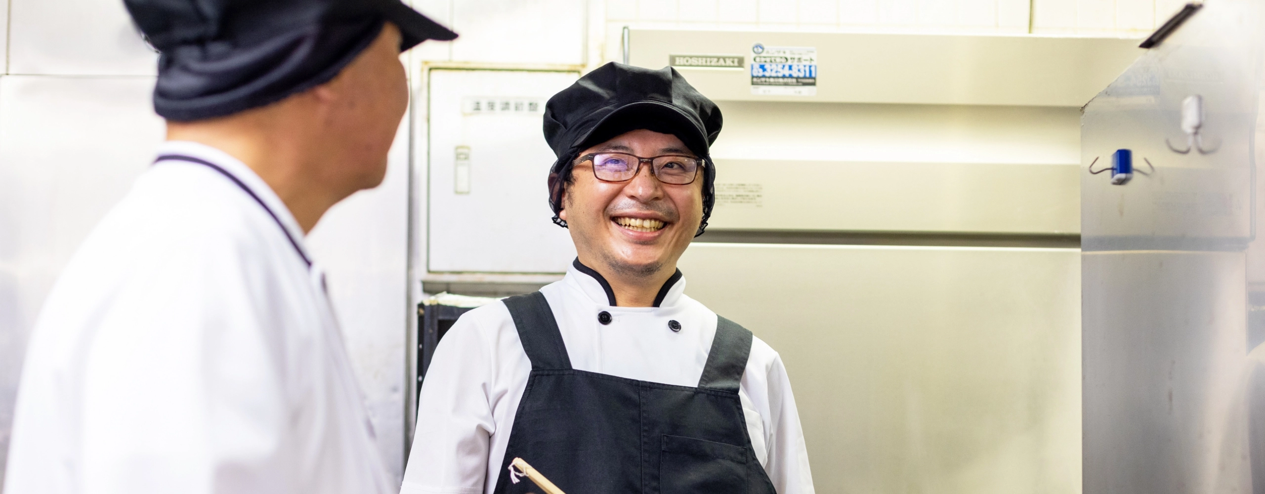 I.T.さんインタビューキービジュアル　厨房でスタッフと談笑している写真