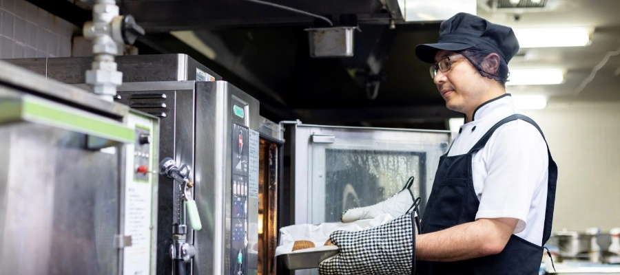 I.T.さん仕事風景　大きな業務用オーブンからお料理を取り出している写真