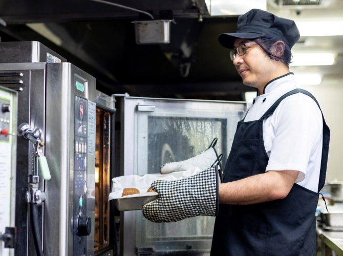I.T.さん仕事風景　大きな業務用オーブンからお料理を取り出している写真