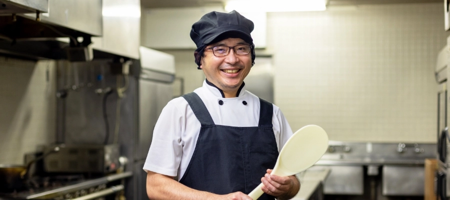 I.T.さん仕事風景　厨房で大きなしゃもじを持っている写真