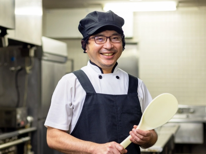 I.T.さん仕事風景　厨房で大きなしゃもじを持っている写真