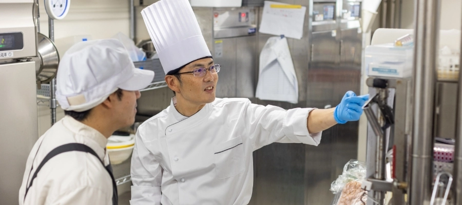 T.Y.さん仕事風景　調理スタッフに機械の使い方を教えている写真