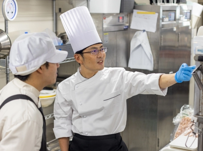 T.Y.さん仕事風景　調理スタッフに機械の使い方を教えている写真