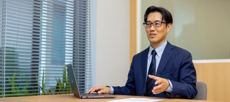 S.K.さん仕事風景　パソコンの横に書類を置いて説明している写真