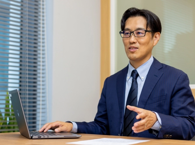 S.K.さん仕事風景　パソコンの横に書類を置いて説明している写真