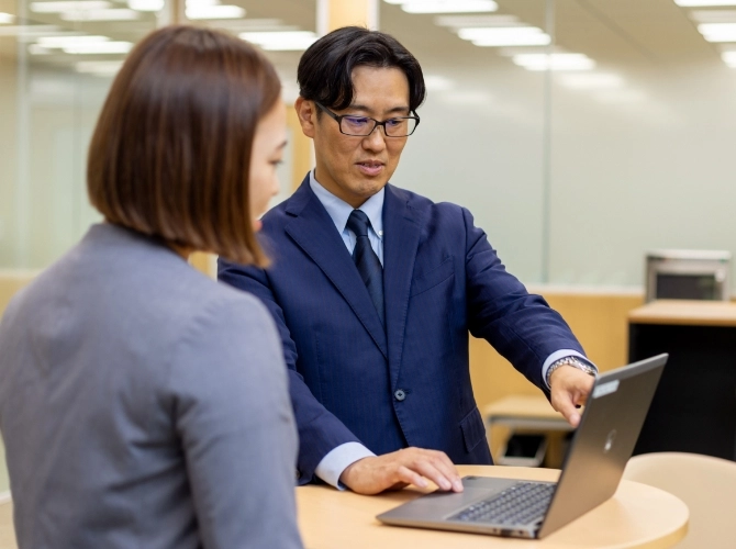 S.K.さん仕事風景　パソコンを指さしながら、スタッフと会話している写真